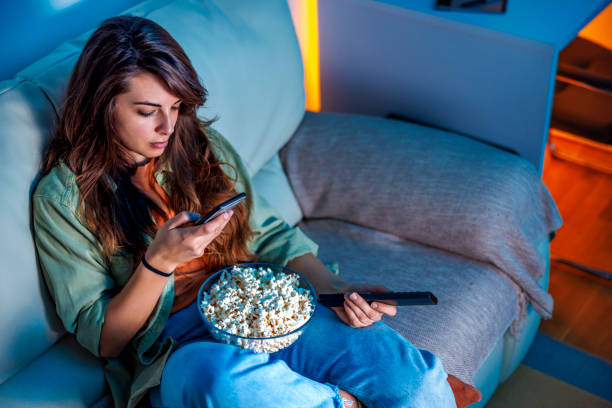 Woman using smart phone and watching TV at home stock photo