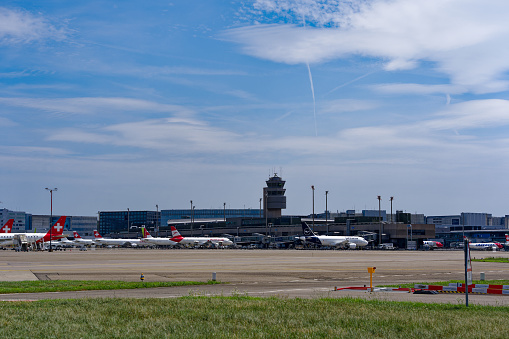 Parked airplanes with air traffic control tower in the background at Zürich Kloten Airport on a sunny summer day. Photo taken July 23rd, 2023, Zurich, Switzerland.