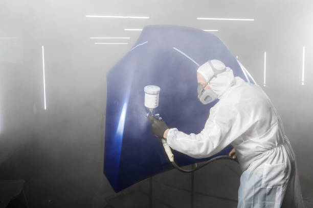 istock Professional bodywork, male car painter in protective mask and workwear apply few layer varnish from spray gun to automobile body parts in garage booth. 1864544365