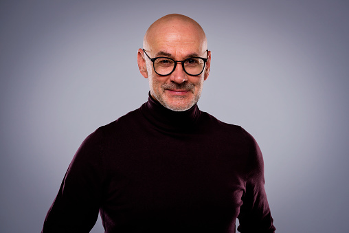 Studio portrait of handsome middle aged man wearing casual clothes while standing at isolated grey background.