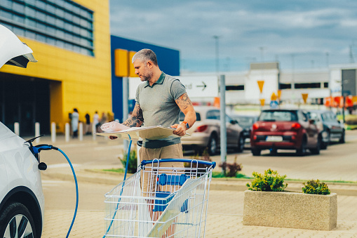 Man charging car at electric vehicle charging station while shopping