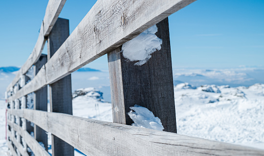 Diminishing perspective of an old wooden fence with frosted snow on its planks, snow covering the mountain under the blue sky