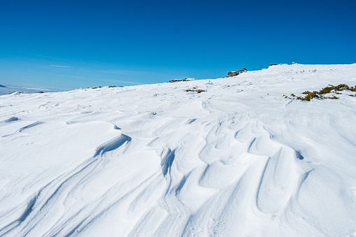 Snow dunes on plateau in the mountains under the clear blue sky in the winter