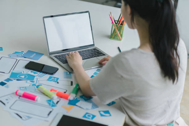 istock Creative UX UI designer working on screens for mobile responsive website development, focusing on UI UX. Developing wireframe sketch layout designs on a smartphone screen. 1864623660
