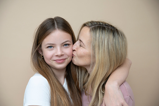 beautiful young, teenager girl together with her beautiful mother in front of brown background