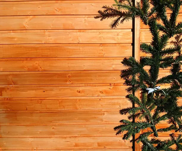 christmas tree fir branches in front of an austrian wooden wall hut in austria in winter, green fir branch from christmas trees, space for Christmas cards Text, wood background for Christmas card invitations and collages