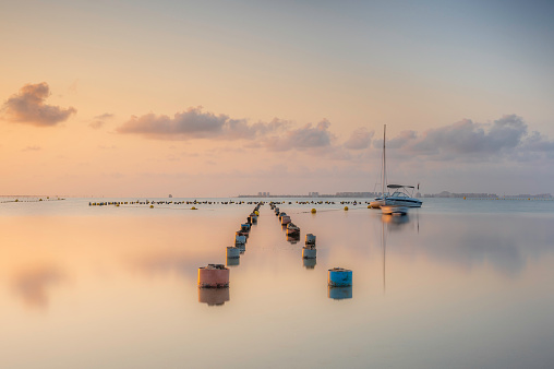 Posts from a ruined jetty, stretching into a calm sea at sunrise. The clouds are reflecting on the glass like ocean