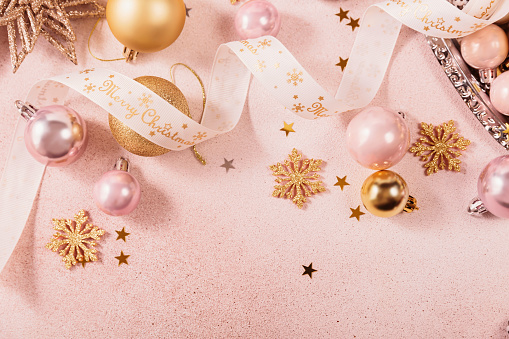 Festive Christmas and New Year background with gold and pink baubles, ribbons and stars. White ribbon with Merry Christmas written. Flat lay, top view with copy space