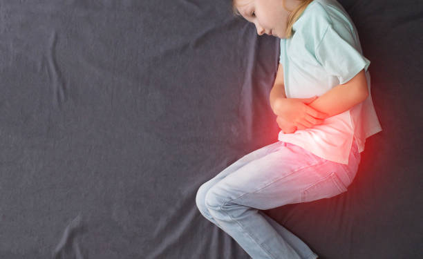 A little caucasian girl of seven years old is lying on the bed with her legs crossed and holding her red belly. Concept of abdominal pain due to poisoning, rotavirus infection. Indigestion, bloating. Copy space for text, view from above una niña caucásica de siete años está acostada en la cama con las piernas cruzadas y sosteniendo su vientre rojo. concepto de dolor abdominal por intoxicación, infección por rotavirus. indigestión, hinchazón. espacio de copia para texto, espasmo. v