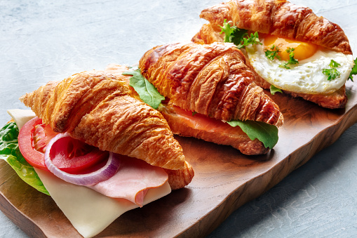 Croissant sandwich variety. Various stuffed croissants on a wooden cutting board. Rolls filled with ham, salmon, egg