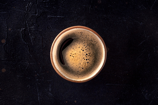 A cup of black coffee with froth, overhead flat lay shot on a dark background