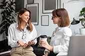 Cheerful lady coworkers enjoying coffee break, two businesswomen talking, meeting and chatting in office