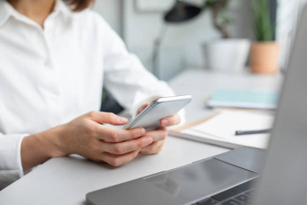 istock Closeup shot of woman office worker using smartphone while sitting at table with laptop, selective focus 1864687125