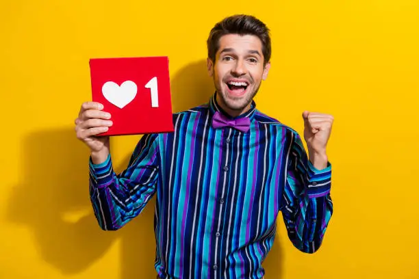 Photo of Photo of satisfied ecstatic funny man with stubble dressed striped shirt get one more like on post isolated on yellow color background