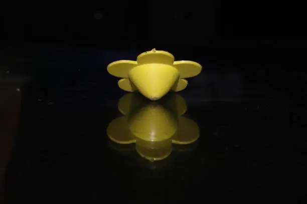 A Small Flower Shaped plastic hand spinning top toy on a black isolated background, reflection