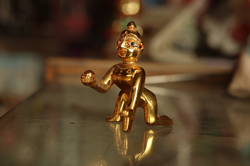 A shiny brass figurine of laddu Gopal or lord Krishna on a glass surface with background blur, closeup side profile