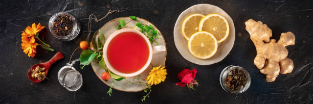 Tea with herbs, fruits, and flowers panorama, overhead flat lay shot Tea with herbs, fruits, and flowers panorama, overhead flat lay shot on a black background. Healthy natural remedy healthcare fitness and herbal medicine banner set stock pictures, royalty-free photos & images
