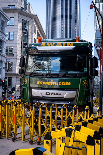 A large and shiny lorry parked in a narrow street in the City of London, delivering to a building where construction work is underway.