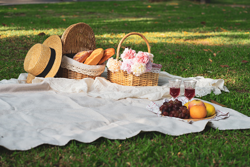 Close up of food drinks and a picnic basket on blanket in the grass in a summer park. Concept of leisure and family weekend