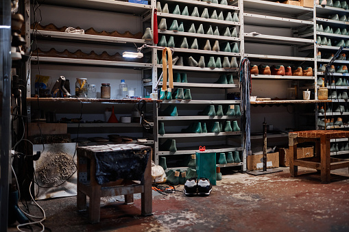 Part of spacious workshop of shoemakers with small and narrow tables, two stools and long shelves with workpieces of footwear