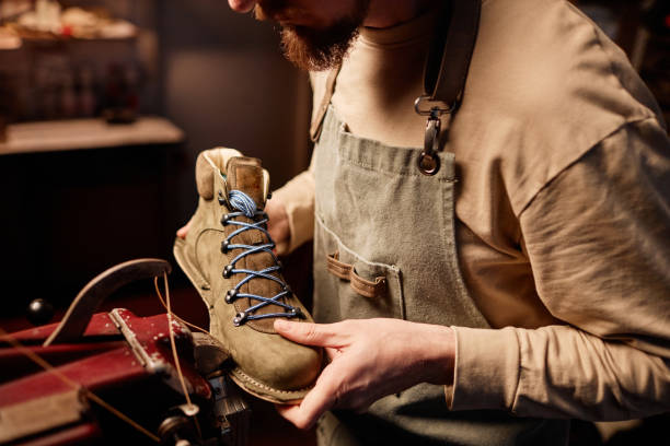 Young shoemaking master sewing upper part of boot workpiece together with sole