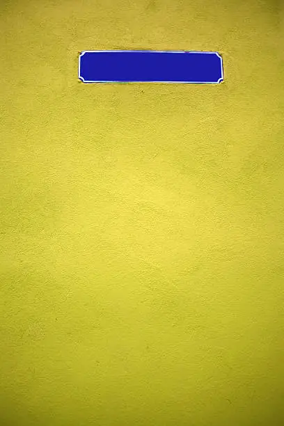 Color shot of an empty blue street sign on a yellow wall