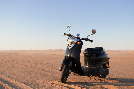 Walvis Bay, Namibia -12 December, 2023:The Retro black scooter at sunset in the golden sand of the Namib Desert