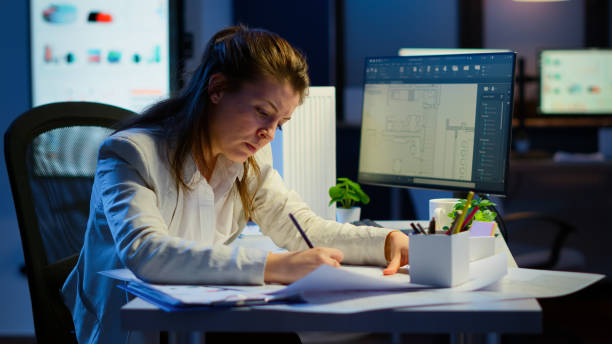 istock Overworked woman architect analysing and matching blueprints 1864852570