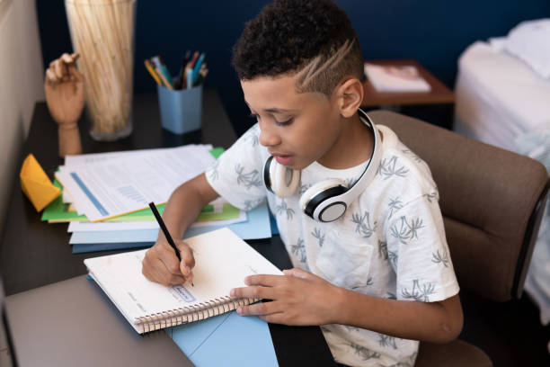 istock Young boy studies and writes at the table in his room 1864866497