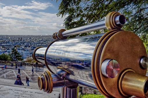 Sacré-Coeur Basilica, Montmartre, Paris, France - An old fashioned coin operated viewing telescope made of steel and brass metal at the top of the hill outside the church looking towards a panoramic view of the city