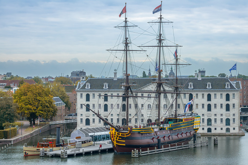 Netherlands, Amsterdam - September 24, 2021: Cloudy summer day. Medieval three-masted sailing ship and the building of the Maritime Museum