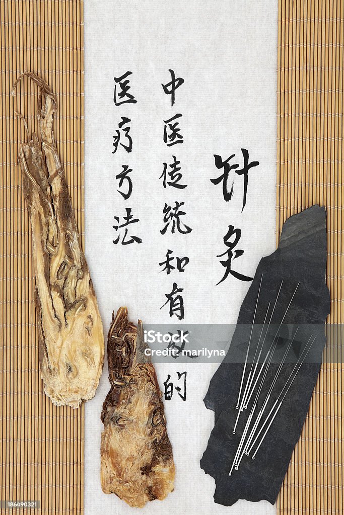 Angelica Root Acupuncture needles with angelica herb root and mandarin script on rice paper over bamboo. Dang gui pian. Translation describes acupuncture chinese medicine as a traditional and effective medical solution. Acupuncture Stock Photo