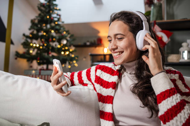 Portrait of a young woman with wireless headphones surfing the net on the smart phone while sitting on the couch in the living room