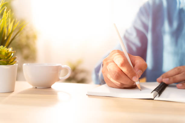istock Close-up of man hand using writing pencil memo on notebook paper or letter, diary on table desk office. Workplace for student, writer with copy space. business working and learning education concept. 1864955884