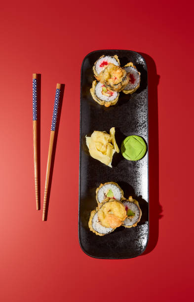 overhead shot of a baked tempura roll with avocado, eel, and tobiko caviar on a black plate. the stark red background creates a striking contrast - 16637 imagens e fotografias de stock