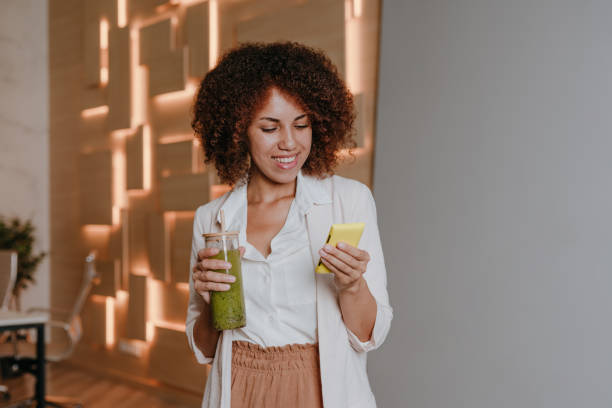 istock Woman using smartphone drinking green smoothie with bamboo straw in the office 1864998285