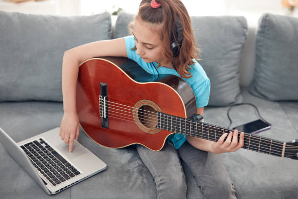 istock Kid playing guitar and watching video lessons on a laptop. 1864999360