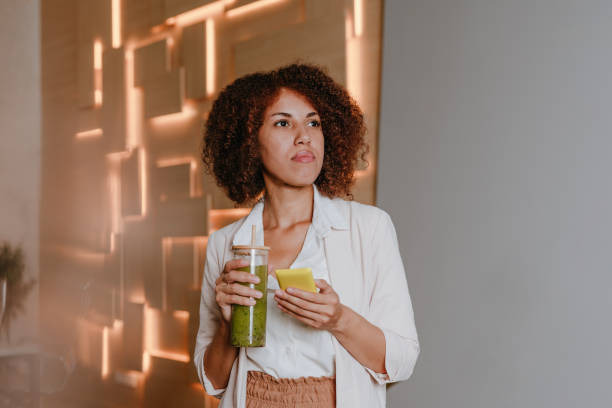 istock Woman using smartphone drinking green smoothie with bamboo straw in the office 1865000468