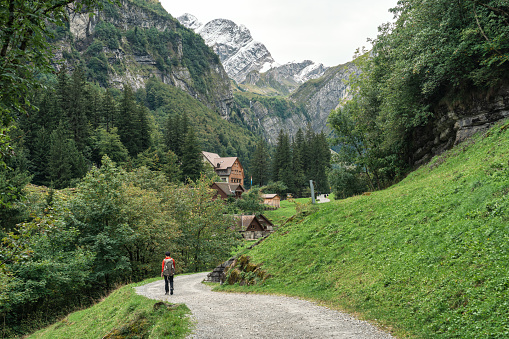 Beautiful view of rustic village and male backpacker walking in Alpstein mountain between trail to Seealpsee lake during summer at Appenzell, Switzerland