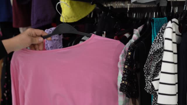 Woman Buying Used Sustainable Clothes From Second Hand Charity Shop, Looking at pink T-shirt