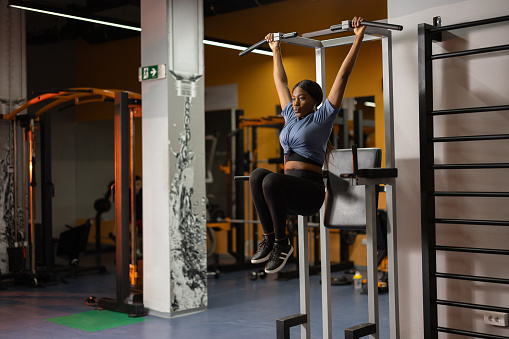 Beautiful black woman exercising abdominal muscles while hanging on horizontal bar in the gym