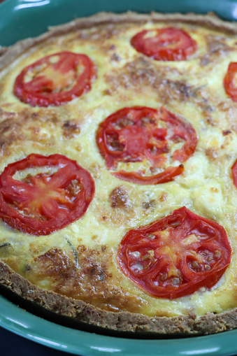 Stock photo showing close-up, elevated view of a pastry crust, homemade, Quiche Lorraine topped with tomato slices.
