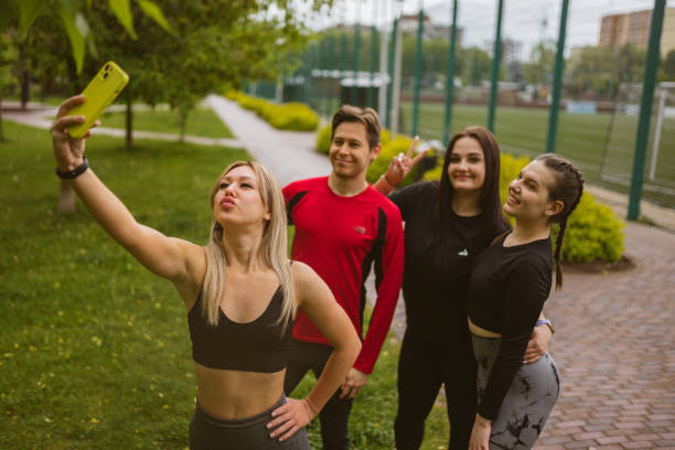 istock Young woman with modern phone makes group selfie in park 1865020882