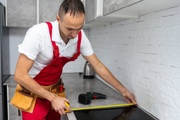 il falegname posiziona il piano cottura a induzione nello spazio previsto per il piano cottura della cucina nella cucina quasi finita. - gas fitter immagine foto e immagini stock