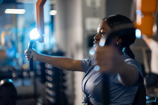 Beautiful black woman working out on fitness exercise equipment at gym with blue neon lights in background
