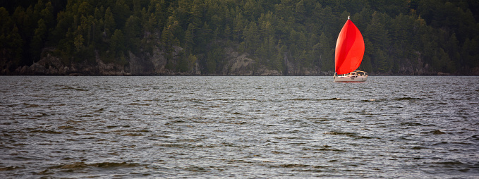 Panoramic view of a lake with a sailboat with red sails