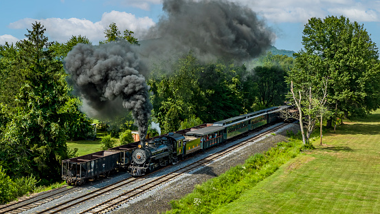 Rockhill Furnace, Pennsylvania, August 5, 2023 - An Aerial View of a Narrow Gauge Steam Passenger Train, Approaching, Blowing Smoke, Passing Coal Hoppers, on a Sunny Summer Day