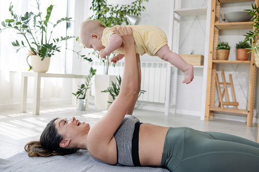 Photo of a mum playing with her baby daughter while exercising on the floor. Harmony.