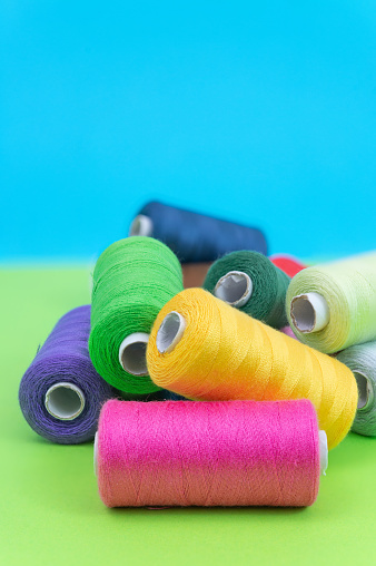 Various spools of sewing cotton thread of different colors on colored background