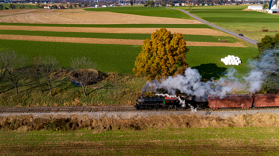 An Aerial Side View of a Steam Freight Train Traveling Thru Farmlands Blowing Smoke on a Sunny Autumn Day